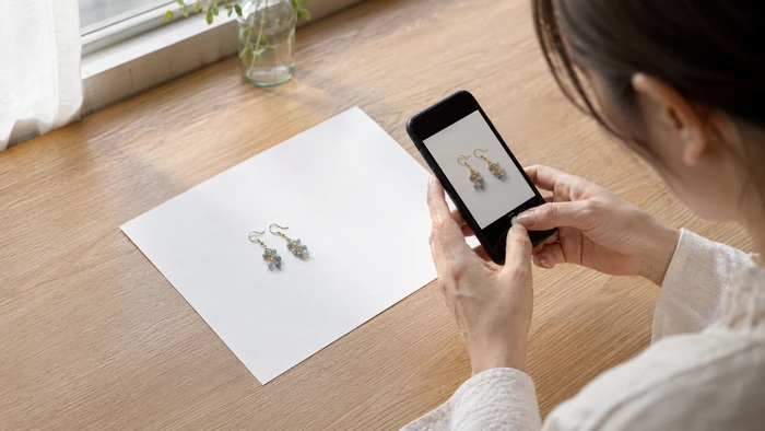 窓辺の自然光と白い紙を使い、スマートフォンでハンドメイドのピアスを撮影する作家