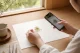 窓辺でハンドメイド作品をスマートフォン撮影する作家の手元